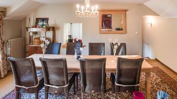 A dining area with a wooden table, wicker chairs, a chandelier, and a patterned rug.