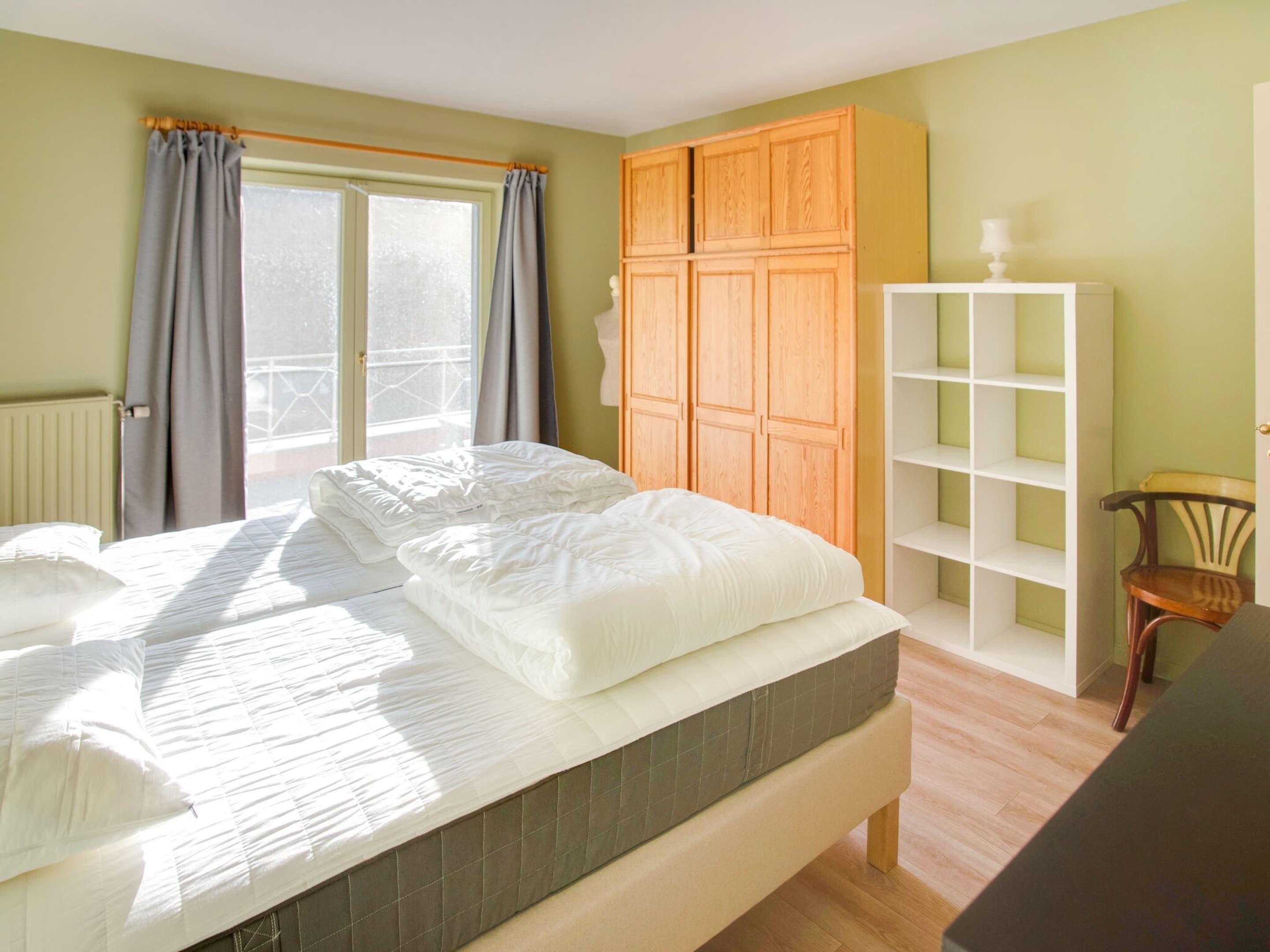 Ein Schlafzimmer mit einem Bett, einem Holzschrank, einem weißen Regalsystem und einem Stuhl.
