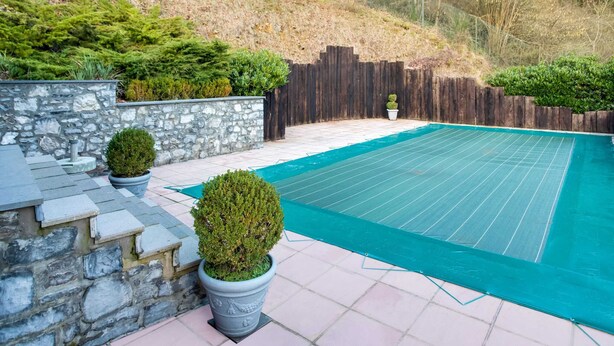 A swimming pool with a stone wall and potted plants.