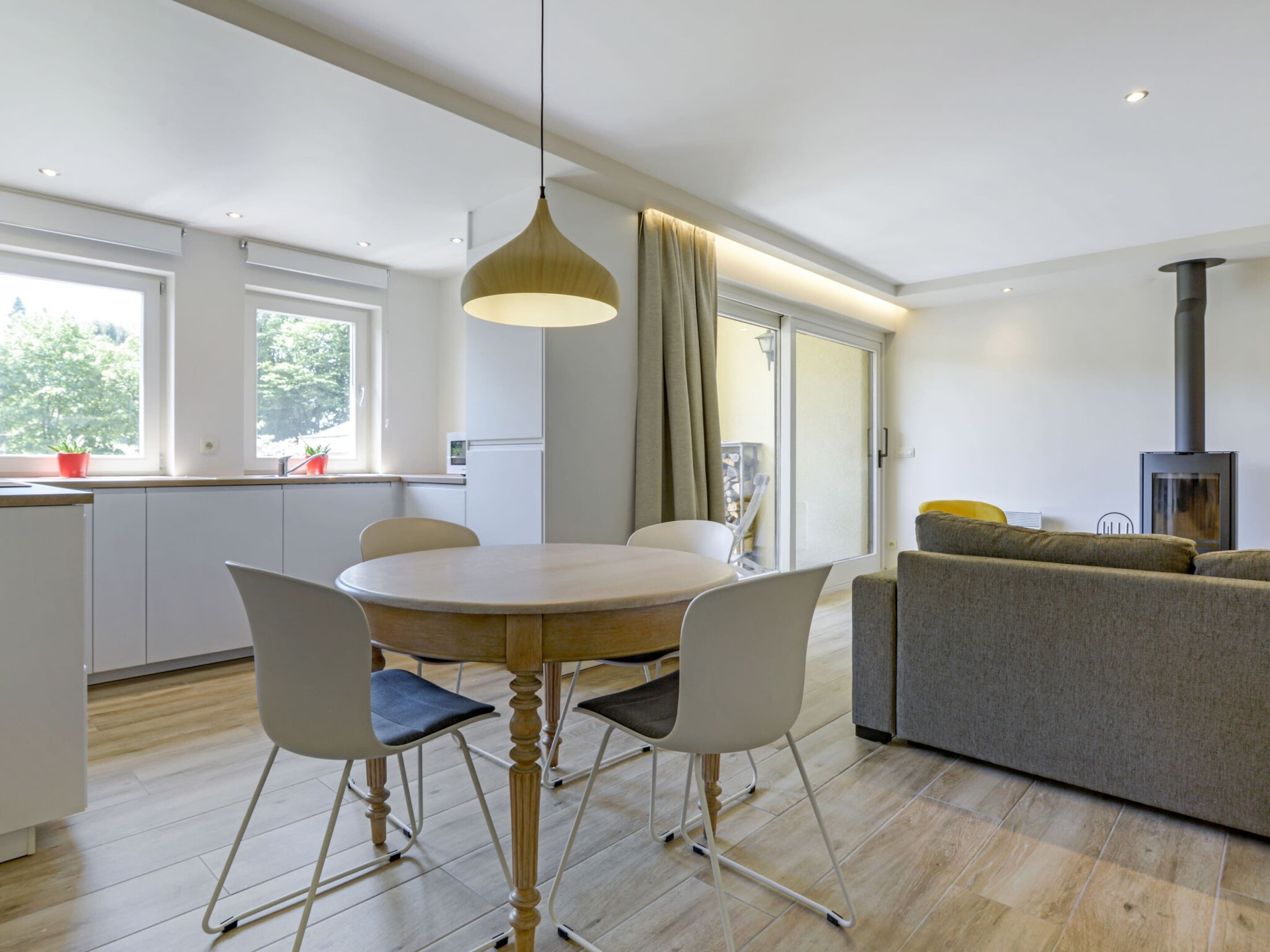 A modern kitchen with white cabinets, a dining table with four chairs, a pendant light, and a built-in stove.