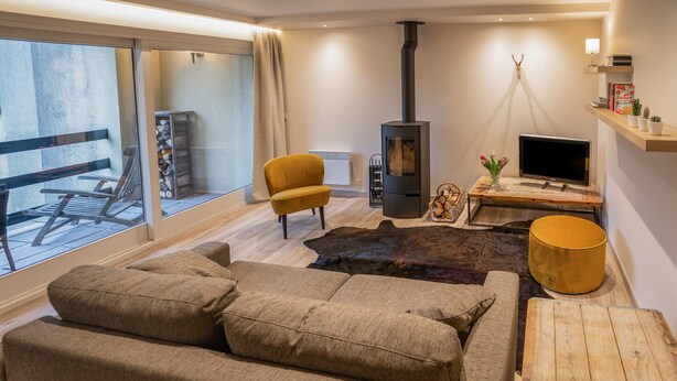 Ein modernes Wohnzimmer mit einer Couch, einem gelben Sessel, einem Fernseher, einem Kamin und einem großen Fenster.