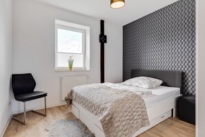 Un dormitorio con cama, una silla, un radiador, una ventana y una pared con diseño a cuadros.