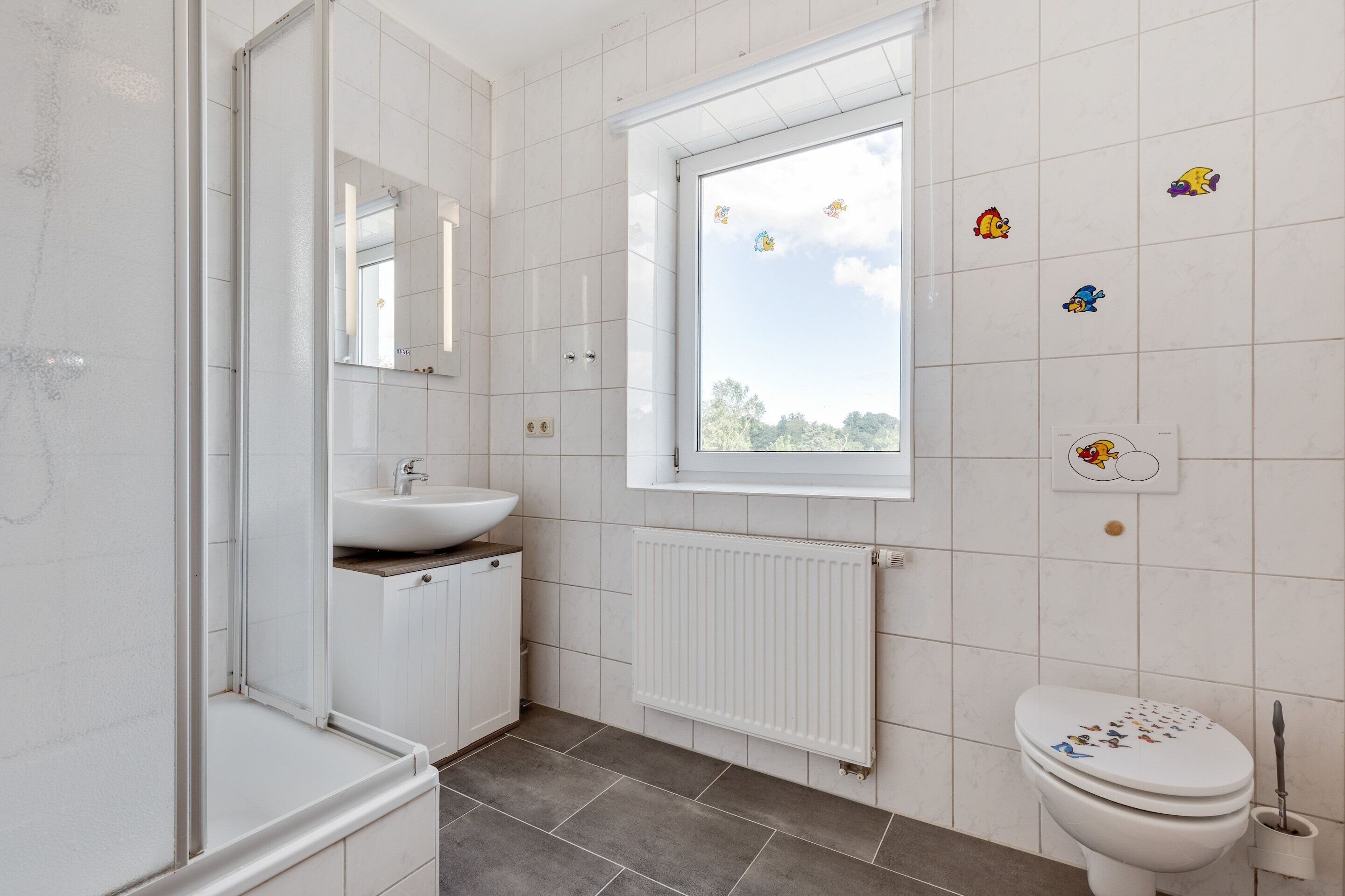 Ein Badezimmer mit Fenster, Waschbecken, Toilette und Spiegel.
