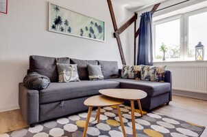 Uma sala de estar moderna com um sofá cinzento, uma mesa de centro redonda de madeira e um tapete estampado.