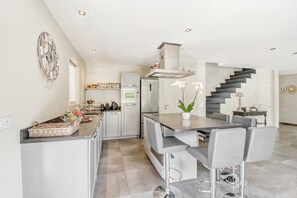 A modern kitchen with a central island, bar stools, a built-in oven, and a staircase leading to another level. - Villa in Le Plan-de-la-tour With Pool (Plan-de-la-Tour)