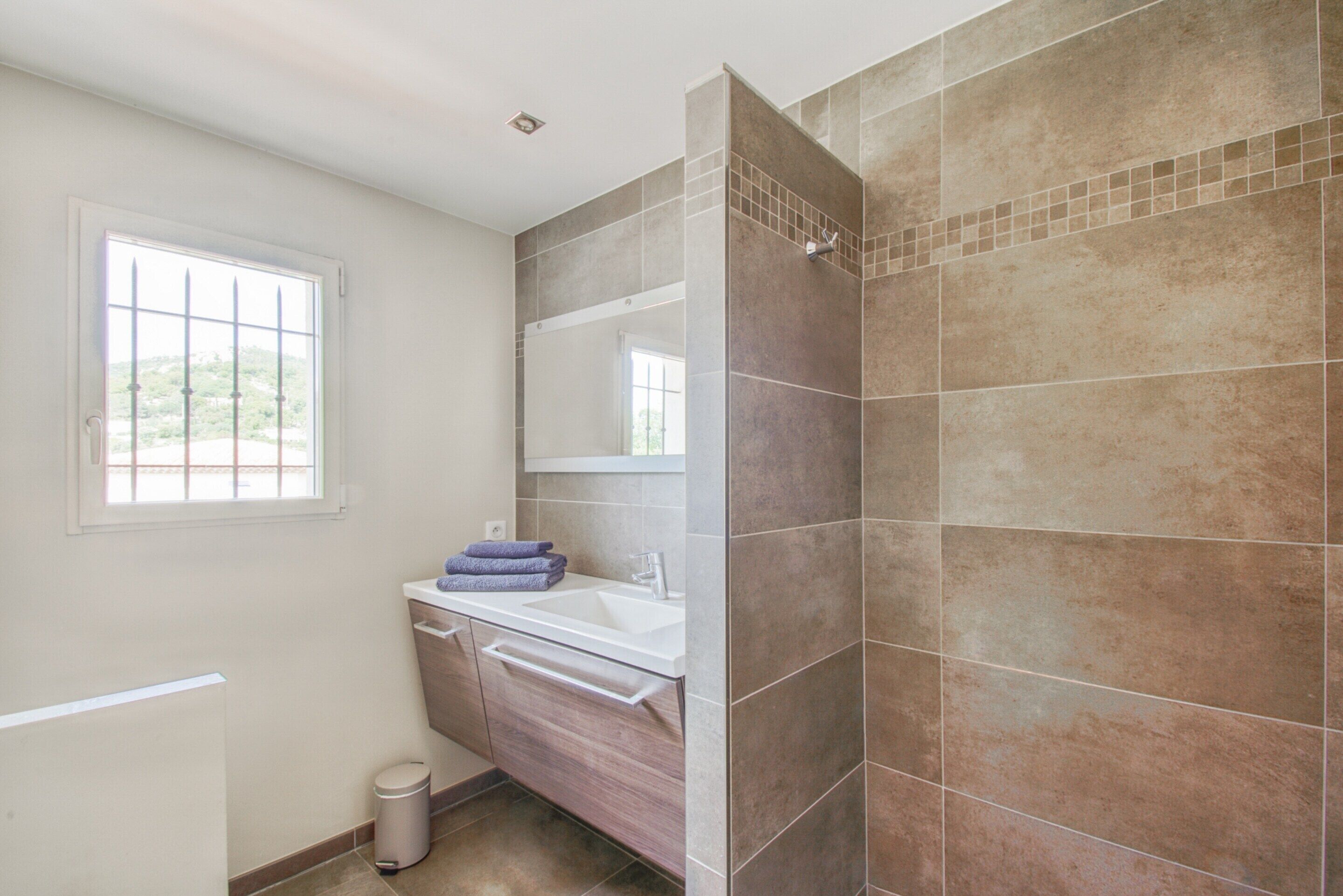 Une salle de bain avec une fenêtre, un lavabo et un espace douche.