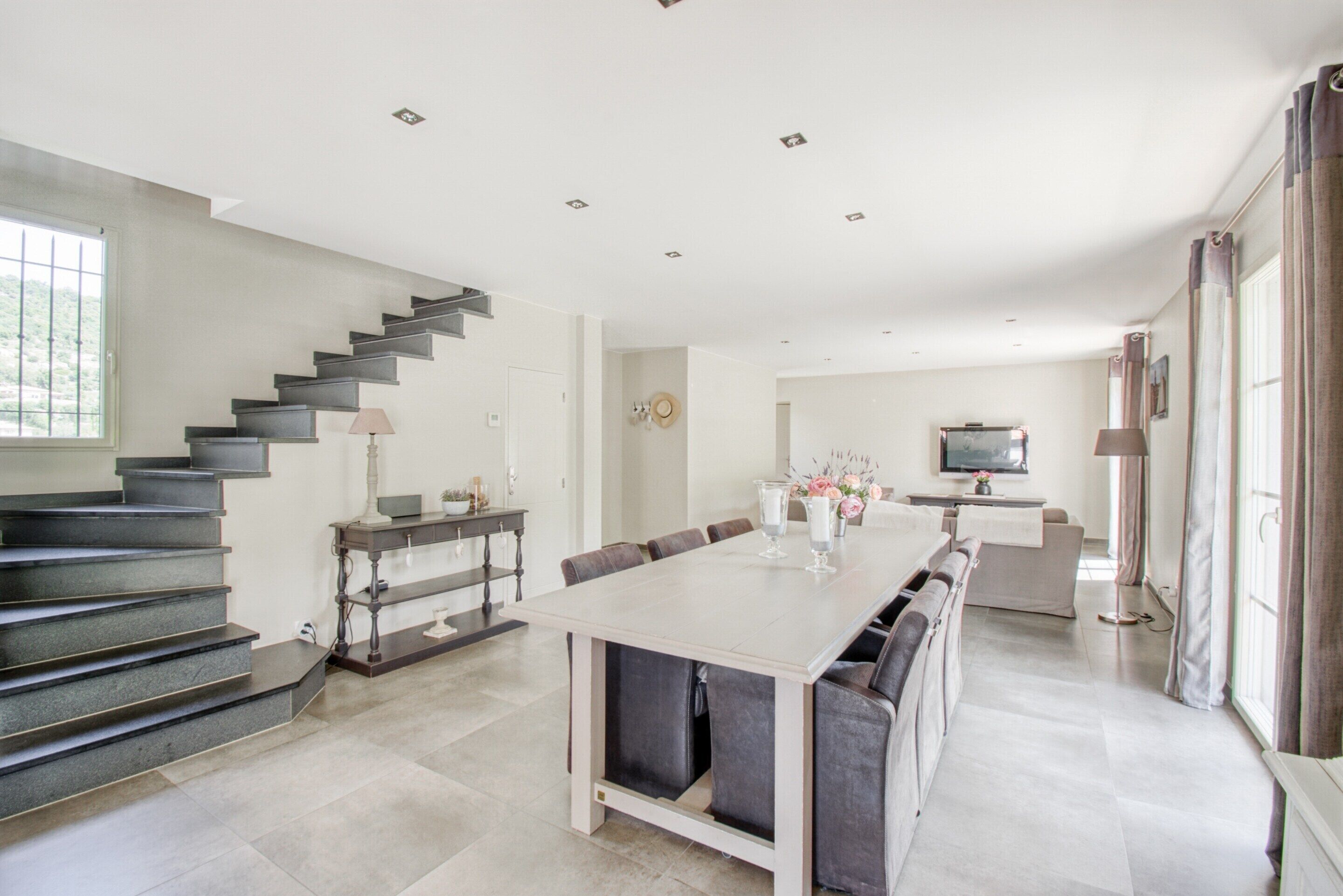 A modern kitchen with a dining area, a staircase, and a television.