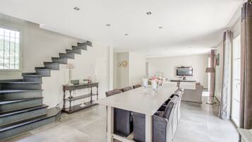 A modern kitchen with a dining area, a staircase, and a television.