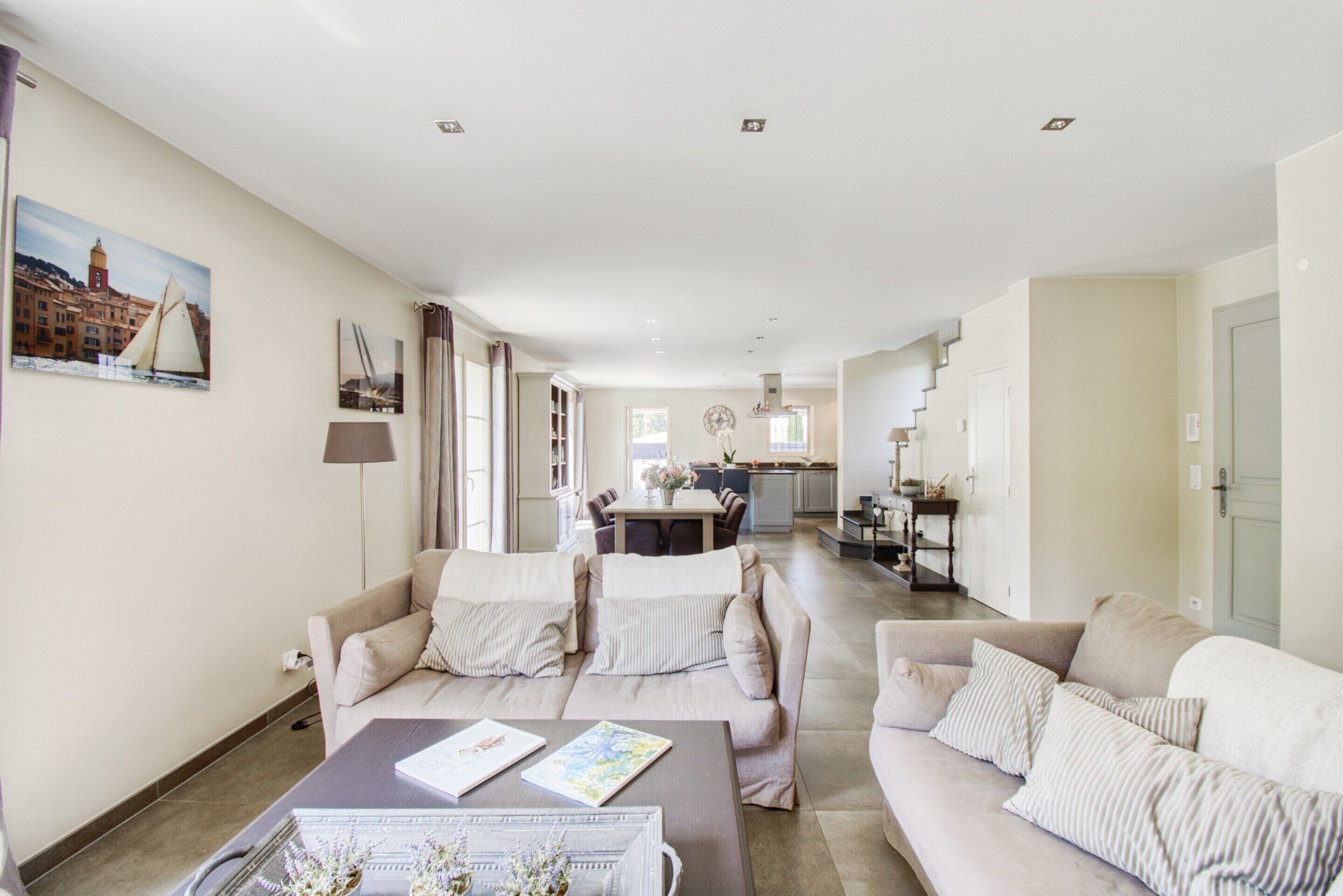 A spacious living area with a sofa set, a coffee table, and a dining area in the background.