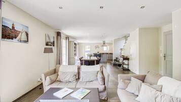 A spacious living area with a sofa set, a coffee table, and a dining area in the background.