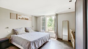 Un dormitorio con cama, ventana, espejo y una obra de arte colgada en la pared.