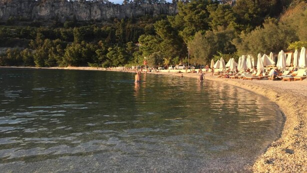 A beach with clear water, a rocky cliff in the background, and beach umbrellas along the shore. - Bonaventura - Countryside Villa near Split with Private Pool (Muc)