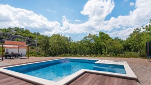 A rectangular swimming pool with a wooden deck, surrounded by a fence and trees. - Bonaventura - Countryside Villa near Split with Private Pool (Muc)
