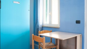 A room with a blue door, a window with white shutters, and a wooden table with two chairs. - Belvilla by OYO Apartment in Policastro Bussentino (Santa Marina)