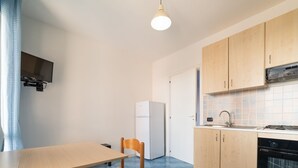 A compact kitchen with a dining table, chairs, a refrigerator, a stove, and a sink. - Belvilla by OYO Apartment in Policastro Bussentino (Santa Marina)
