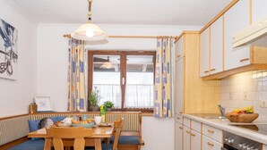 Une cuisine chaleureuse avec des meubles en bois, un four encastré et un coin repas comprenant une banquette et des chaises.