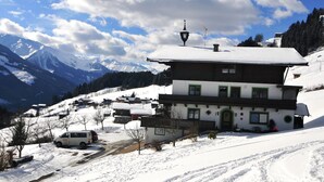 Un chalet à deux étages, avec un toit enneigé, un balcon et une vue sur les montagnes environnantes.
