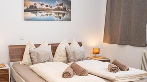 Un lit double avec deux oreillers, une table de chevet avec une lampe et un tableau représentant des montagnes accroché au mur.