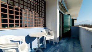 Ein Balkon mit blauen Fliesen, weißen Kunststoffstühlen, einem kleinen runden Tisch und einer Aussicht auf die entfernten Berge.