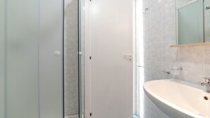 Ein Badezimmer mit einer Duschkabine aus Glas, einem weißen Waschbecken und einem Spiegel darüber.