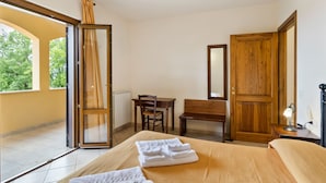 Habitación de hotel con cama, escritorio, silla, armario de madera y ventana con cortinas.