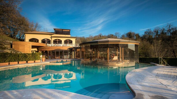 Une piscine à bordures courbes, un belvédère couvert et un bâtiment doté d’arches et d’un balcon.