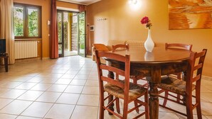 Un coin repas avec une table ronde en bois, quatre chaises en bois, un vase blanc rempli de fleurs et un tableau accroché au mur.