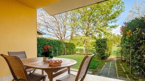 Une terrasse avec une table ronde en bois et quatre chaises, un petit panier en osier et un pot de fleurs orné de fleurs rouges.