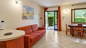 Un salon avec un canapé rouge, une table à manger avec des chaises, un tableau accroché au mur et une porte-fenêtre coulissante donnant sur un jardin.