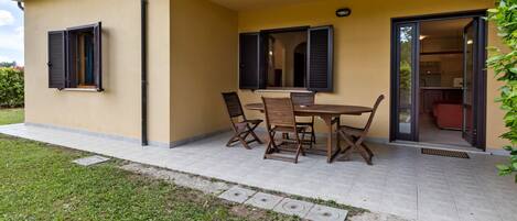 A building with a patio area featuring a table and chairs, a small garden, and a view into the interior.