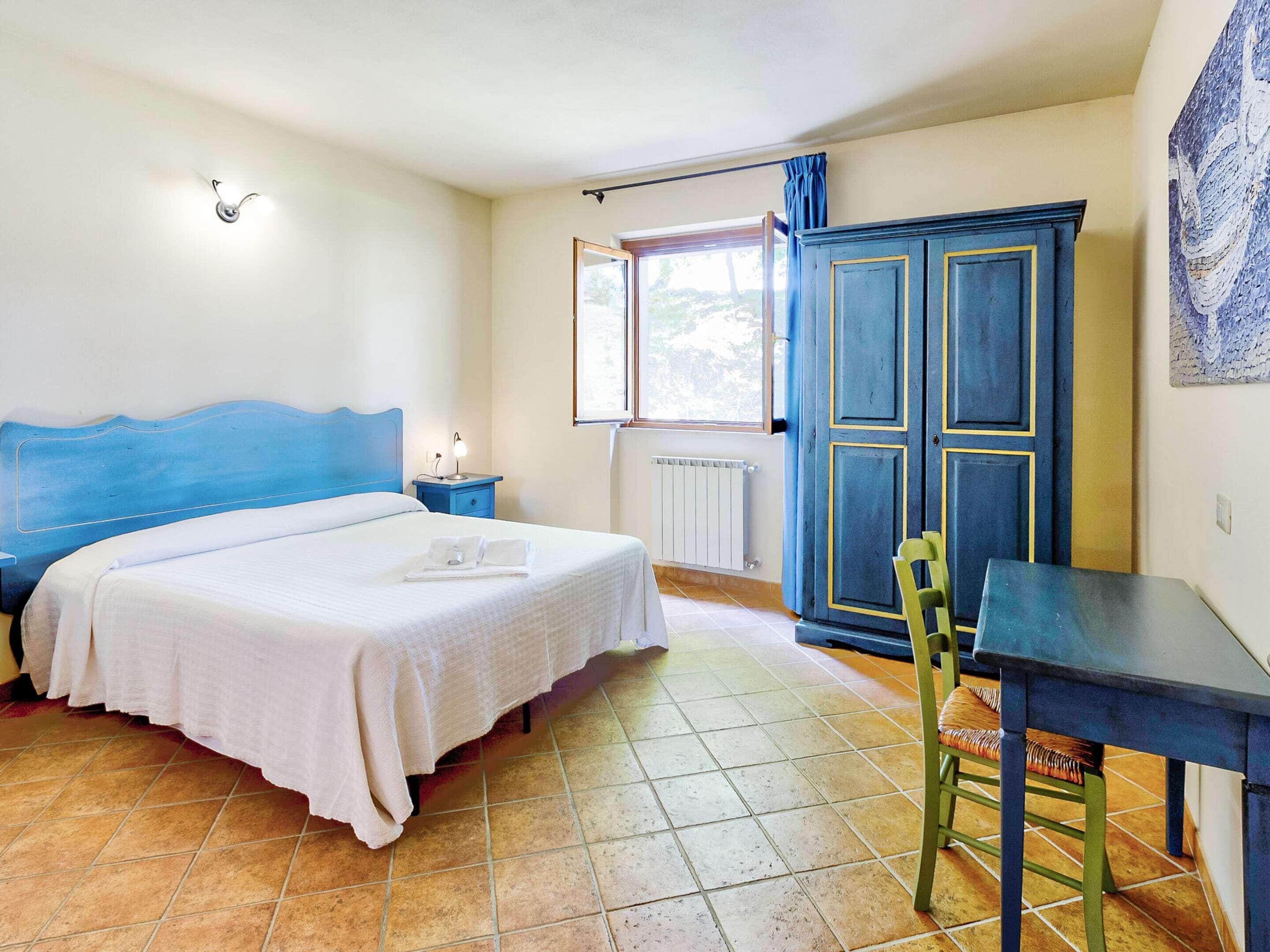 Ein Schlafzimmer mit einem Bett, einem Nachttisch, einem Kleiderschrank, einem Sessel und einem Tisch.