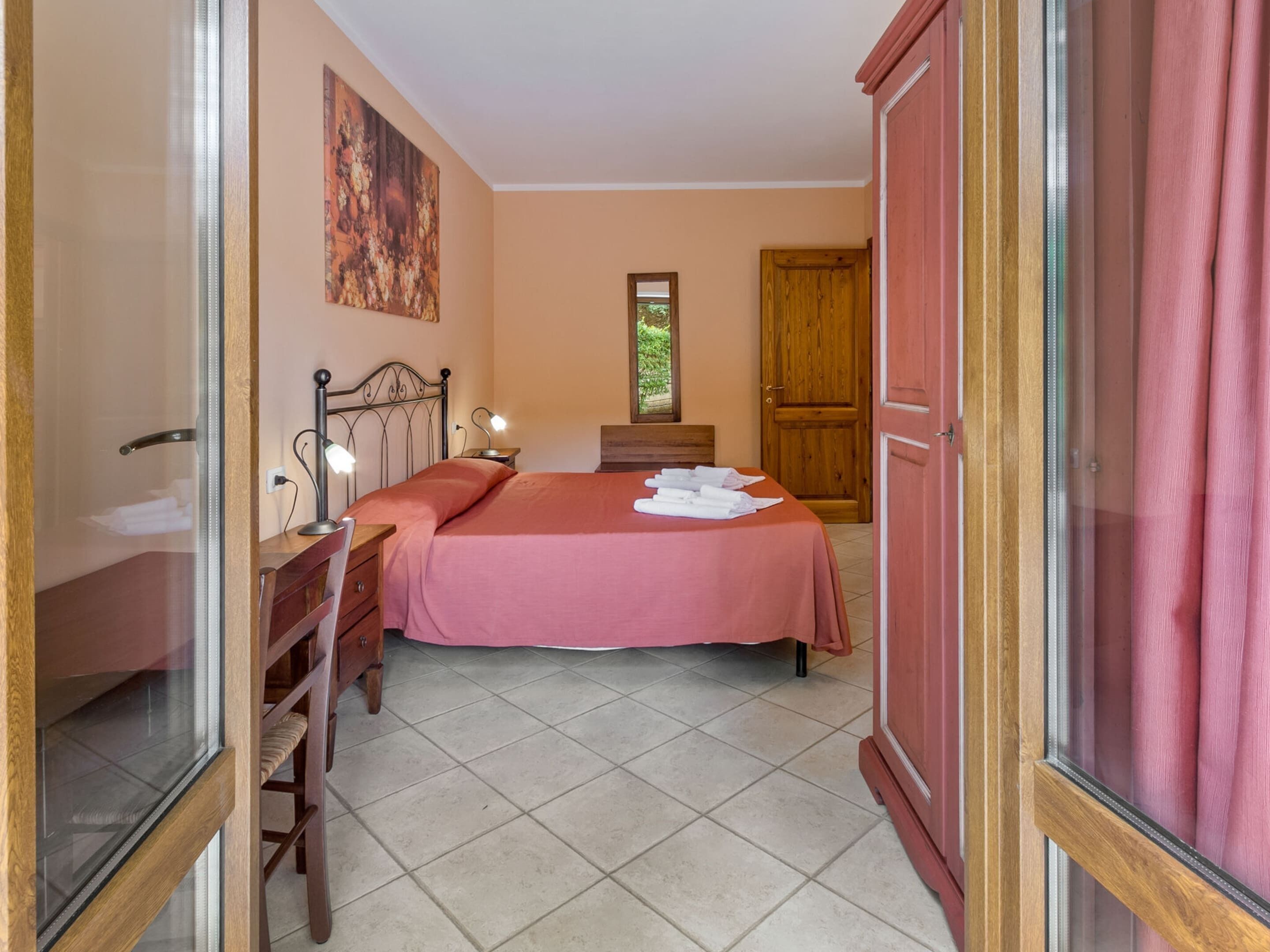 Une chambre à coucher comprenant un lit, une table de chevet, une lampe et une fenêtre donnant sur un paysage verdoyant.