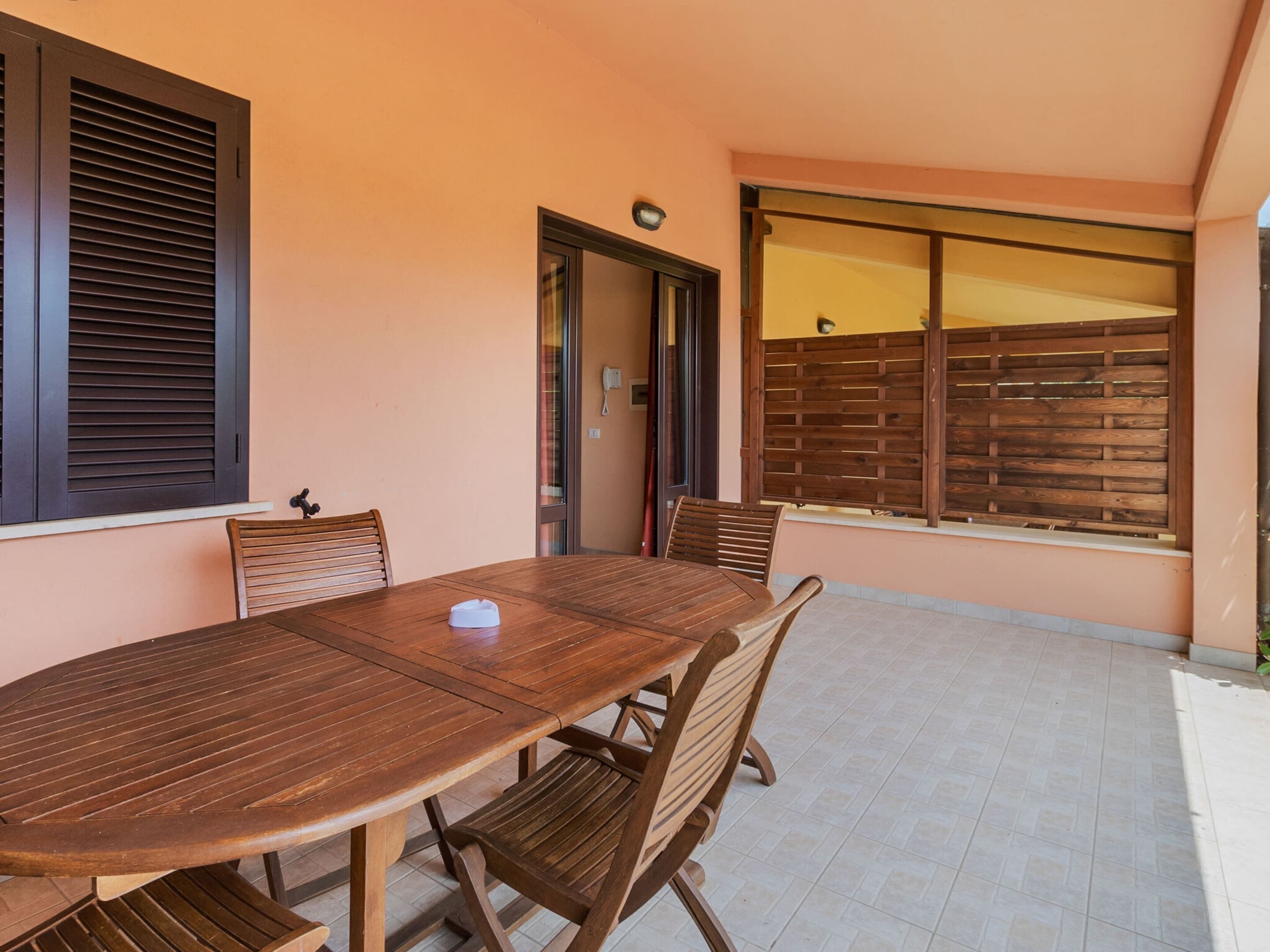 Una mesa de madera con sillas en una habitación con paredes color melocotón y una valla de madera afuera.