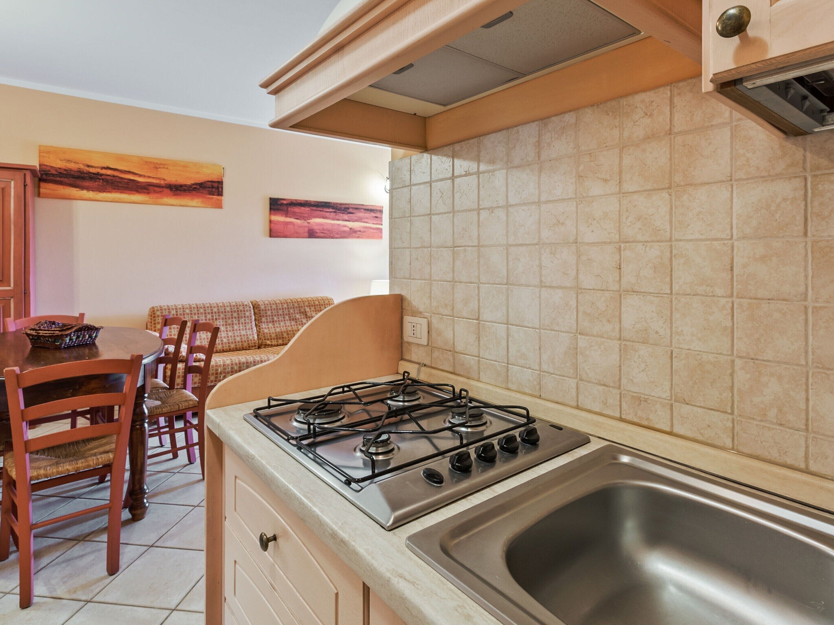A compact kitchen with a gas stove, a stainless steel sink, and a dining area with a table and chairs.
