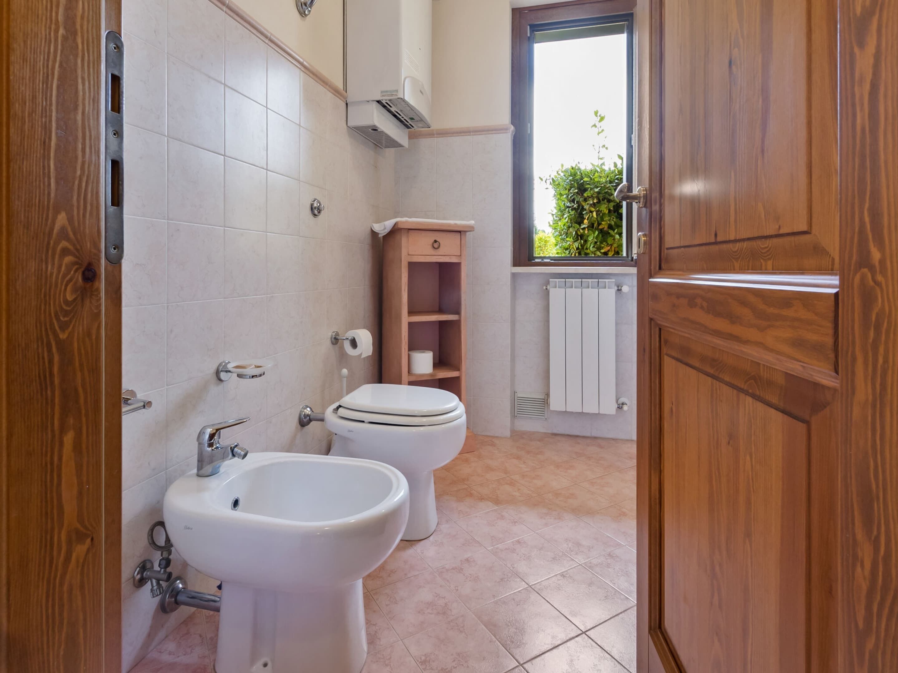 Une salle de bain avec deux toilettes, un bidet et une fenêtre donnant sur un espace verdoyant.