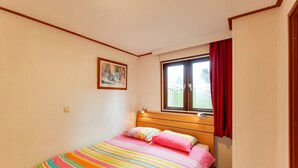 Um quarto pequeno e bem arrumado, com uma cama de solteiro, uma janela com cortinas vermelhas e um quadro na parede.