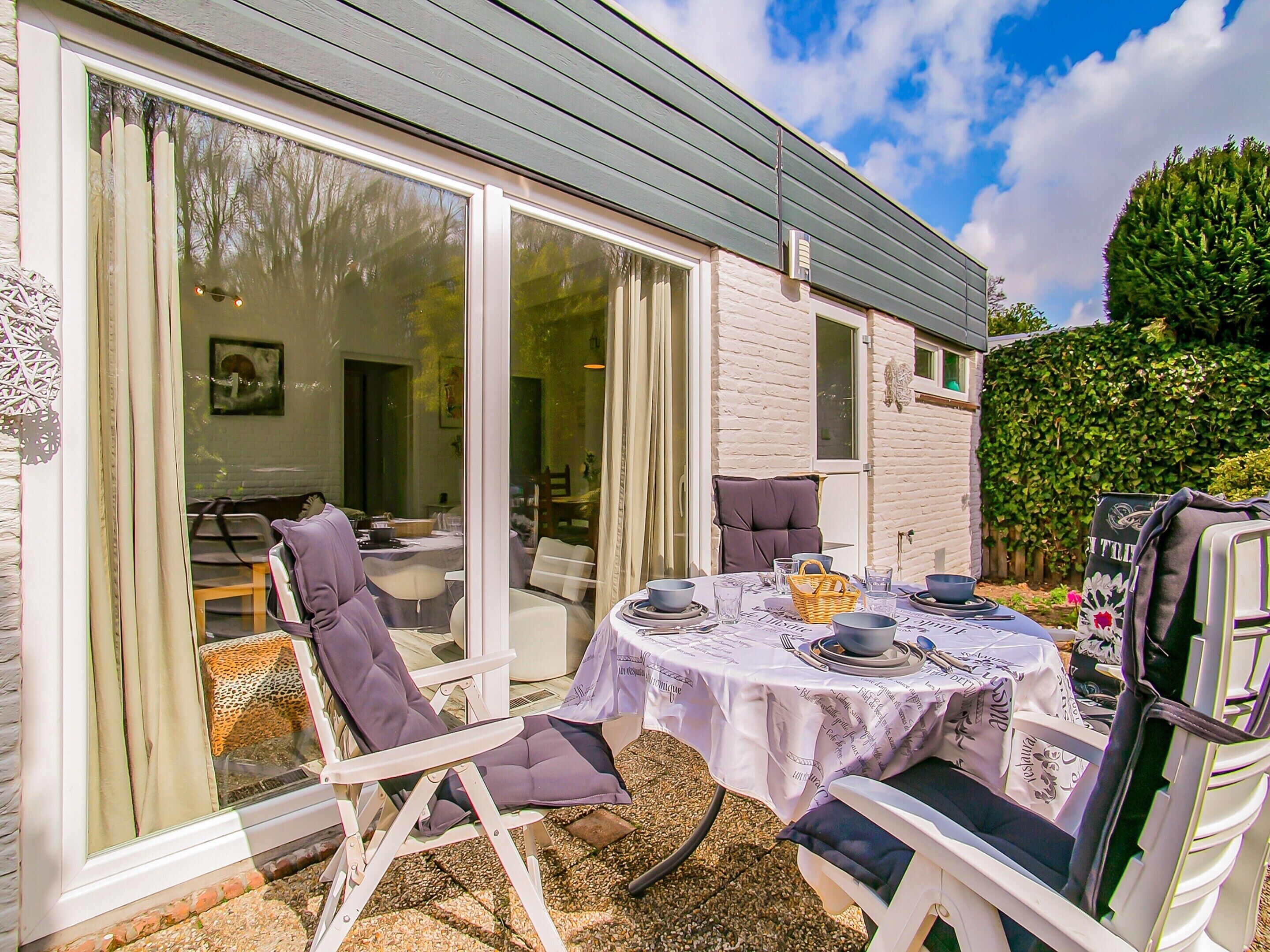 An outdoor dining area with a table set for four, surrounded by white chairs with purple cushions.