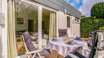 An outdoor dining area with a table set for four, surrounded by white chairs with purple cushions.