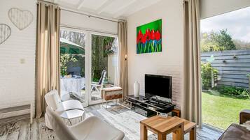 A modern living room with a flat-screen TV, a white leather chair, a wooden coffee table, and a painting of red flowers on the wall.