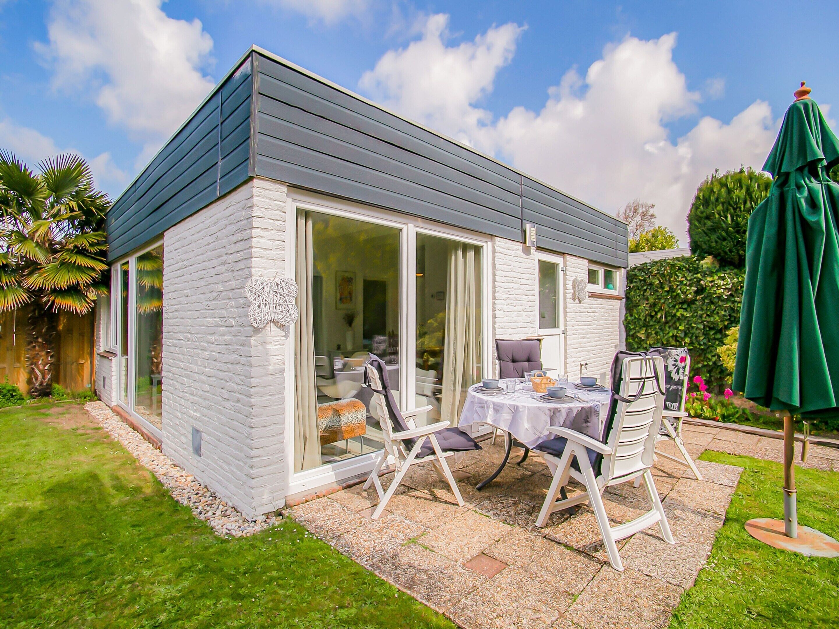 A modern house with a patio area featuring a table and chairs, surrounded by a well-maintained garden.