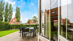 A patio area with a table and chairs, a view of a brick house, and a hedge. - Breskens Haven: Relax, Explore & Dine (Breskens)