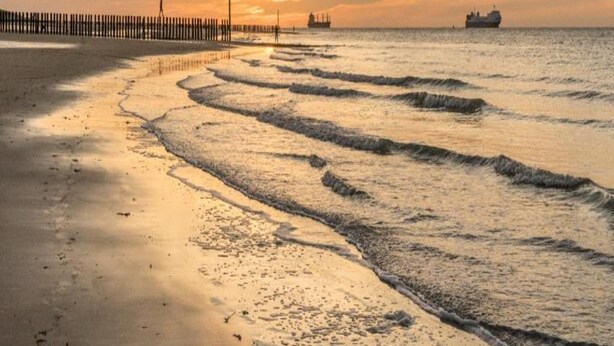 A beach with waves, a pier, and a ship in the distance. - Breskens Haven: Relax, Explore & Dine (Breskens)