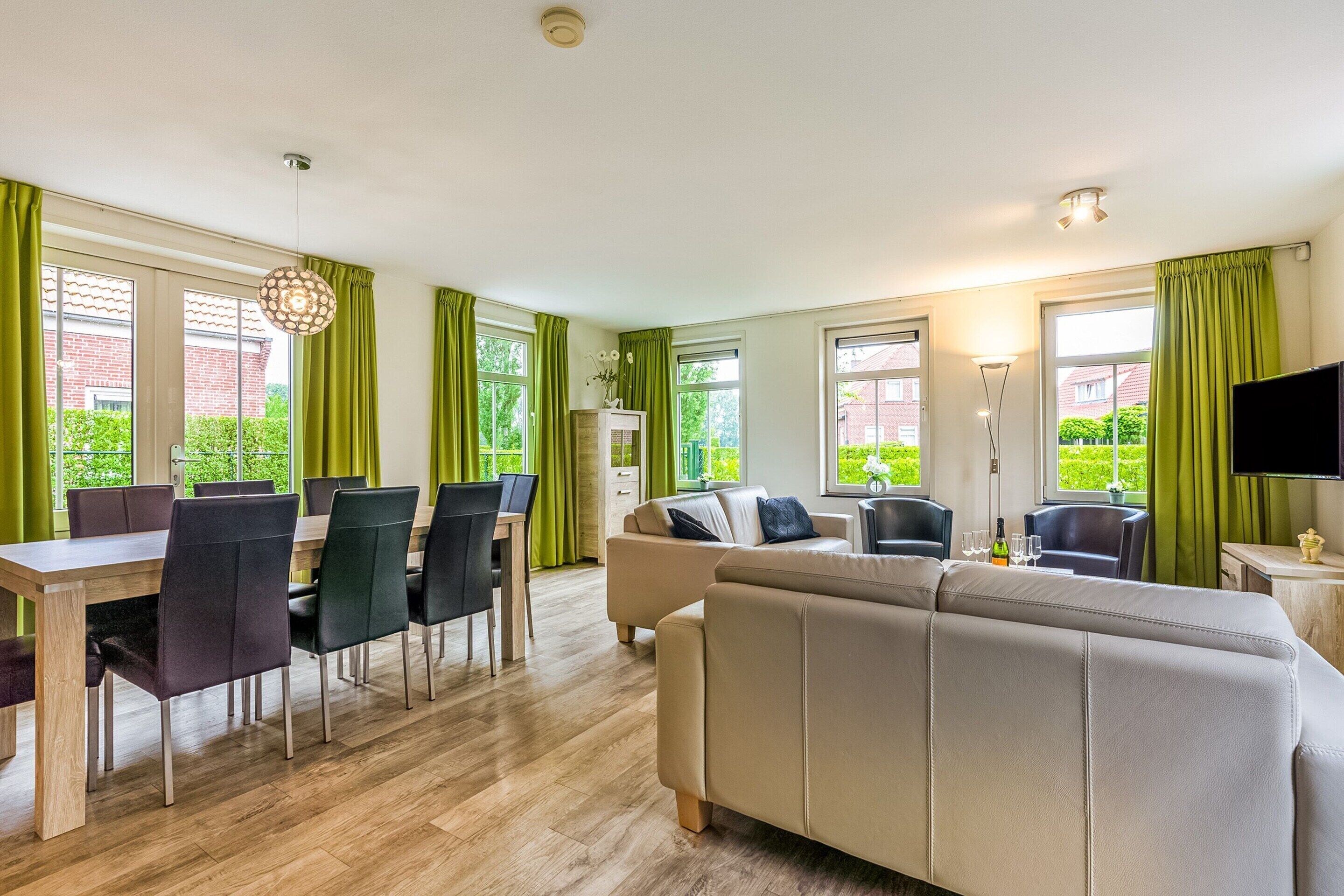A modern living room with a sofa, dining table, and chairs. There is a TV mounted on the wall and a fireplace.