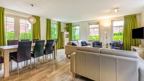 A modern living room with a sofa, dining table, and chairs. There is a TV mounted on the wall and a fireplace. - Breskens Haven: Relax, Explore & Dine (Breskens)