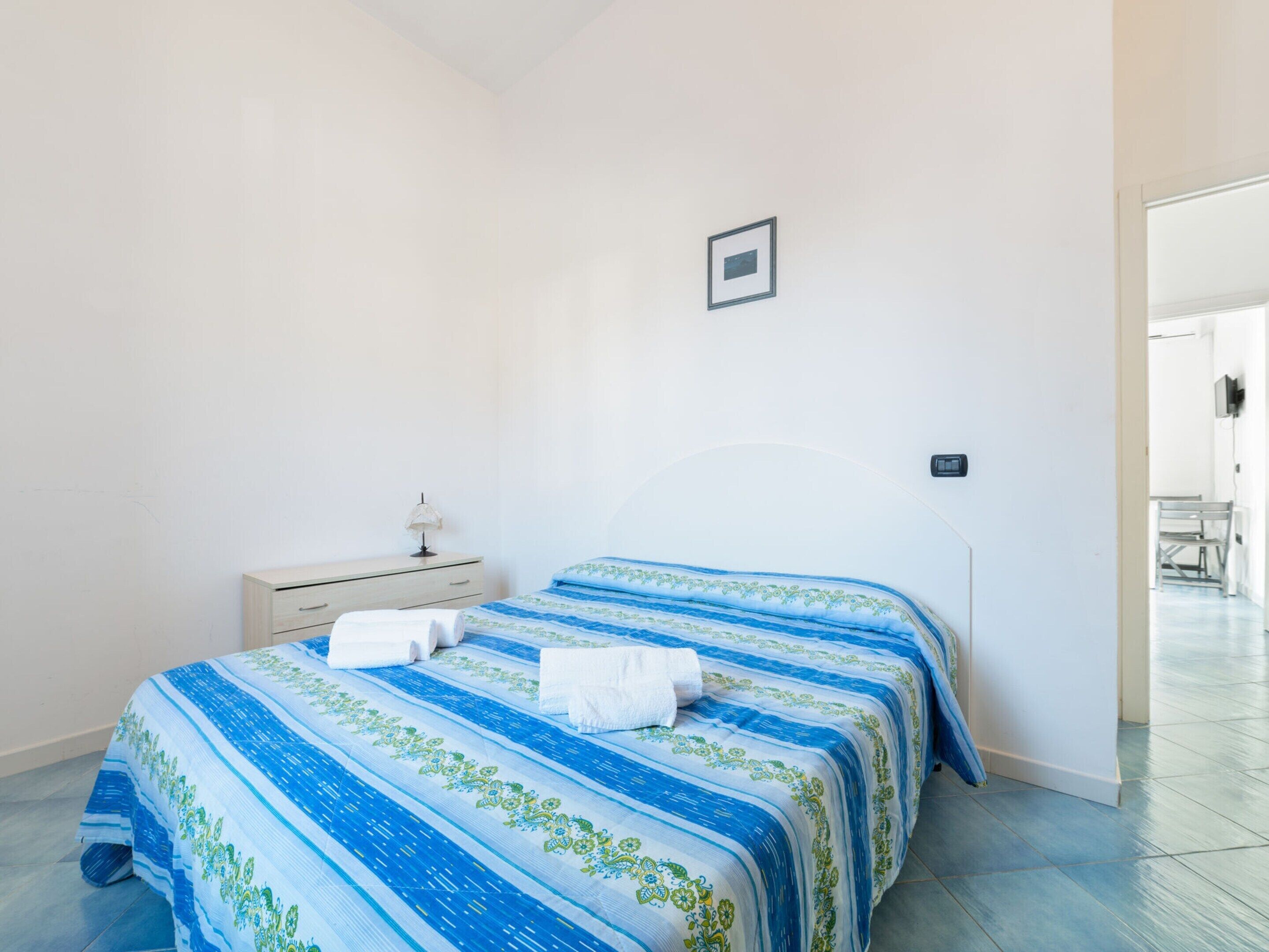A bedroom with two beds, a bedside table, and a lamp.