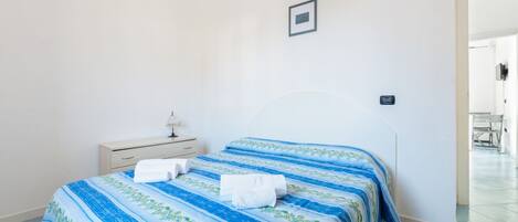A bedroom with two beds, a bedside table, and a lamp.