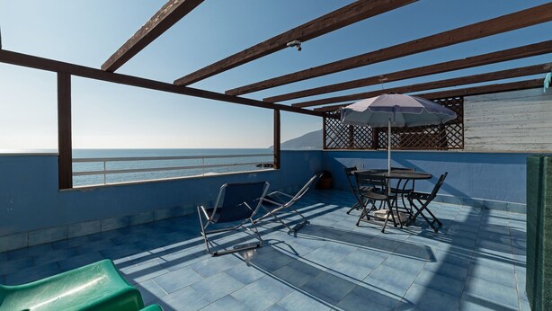 A terrace with a table and chairs, a green chair, and a view of the sea. - Belvilla by OYO Apartment in Policastro Bussentino (Santa Marina)