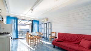 A compact living space with a kitchenette, a dining area with a table and chairs, a red sofa, and a sliding glass door leading to an outdoor area. - Belvilla by OYO Apartment in Policastro Bussentino (Santa Marina)