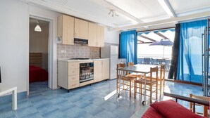 A compact kitchen with wooden cabinets, a built-in oven, and a sink. There is a dining area with a table and chairs, and a red sofa. - Belvilla by OYO Apartment in Policastro Bussentino (Santa Marina)