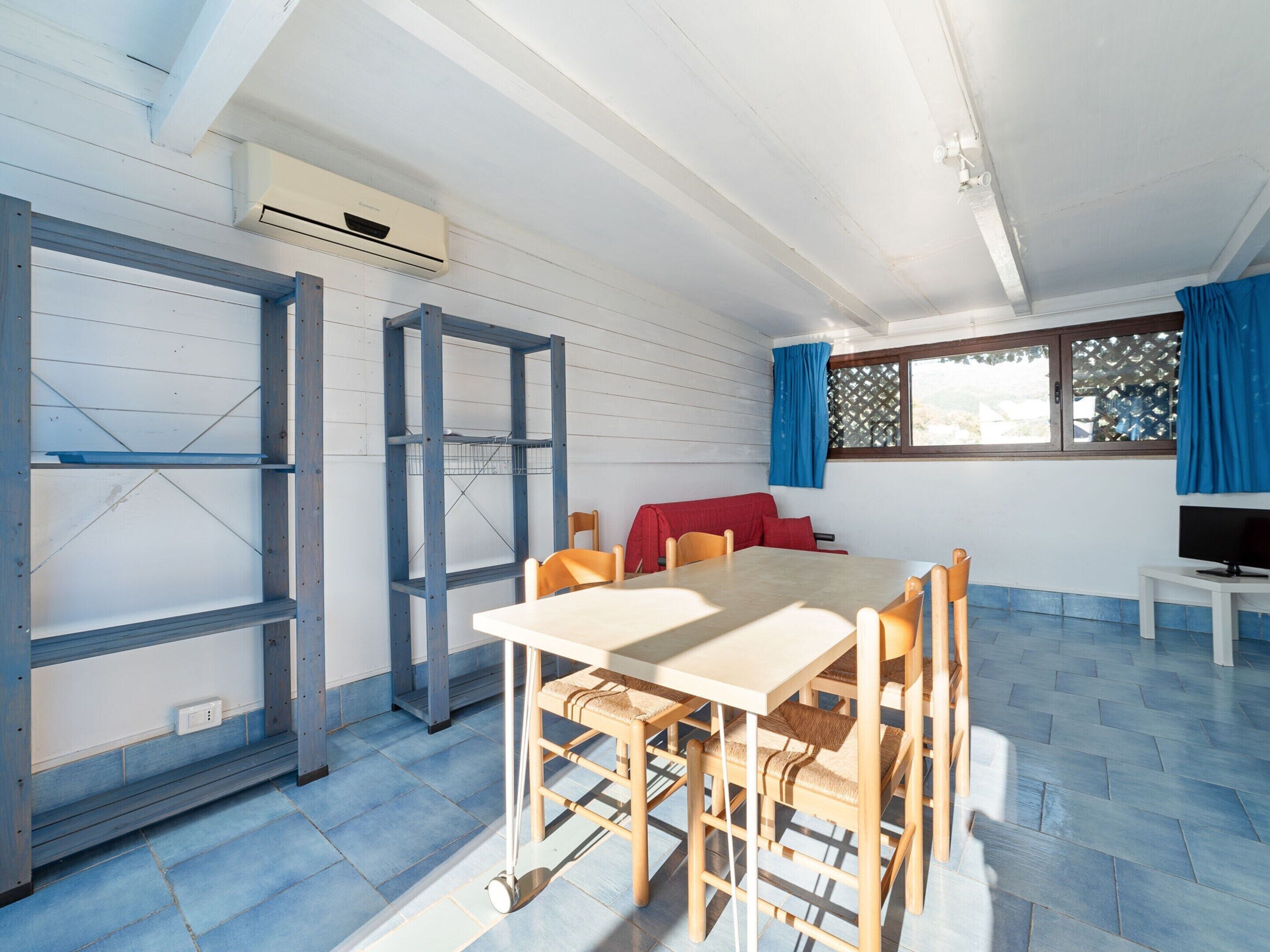 A room with a wooden table and chairs, a red couch, a TV, and a window with blue curtains.